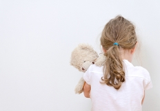 Una bambina, di spalle, tiene in braccio un orsetto di peluche 