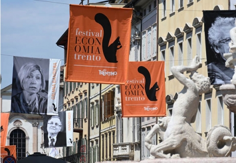 Cartelloni arancioni con il logo e la scritta del festival dell'economia e con i relatori all'evento lungo via Belenzani