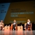 Le relatrici e la coordinatrice sul palco del Teatro Sociale, sedute con sedie arancioni davanti a un maxischermo